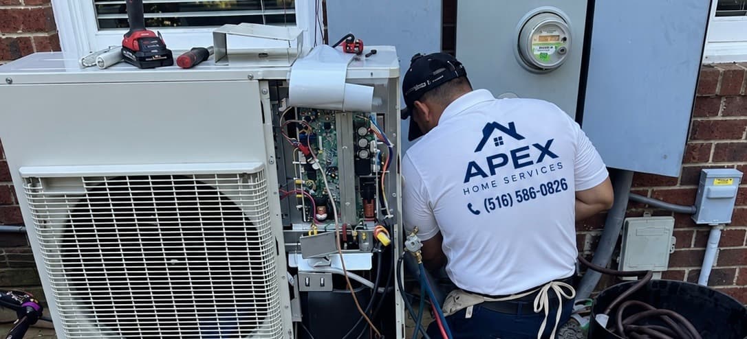 Apex technician connecting refrigerant gauges to an outdoor heat pump unit, head and shoulders fully visible